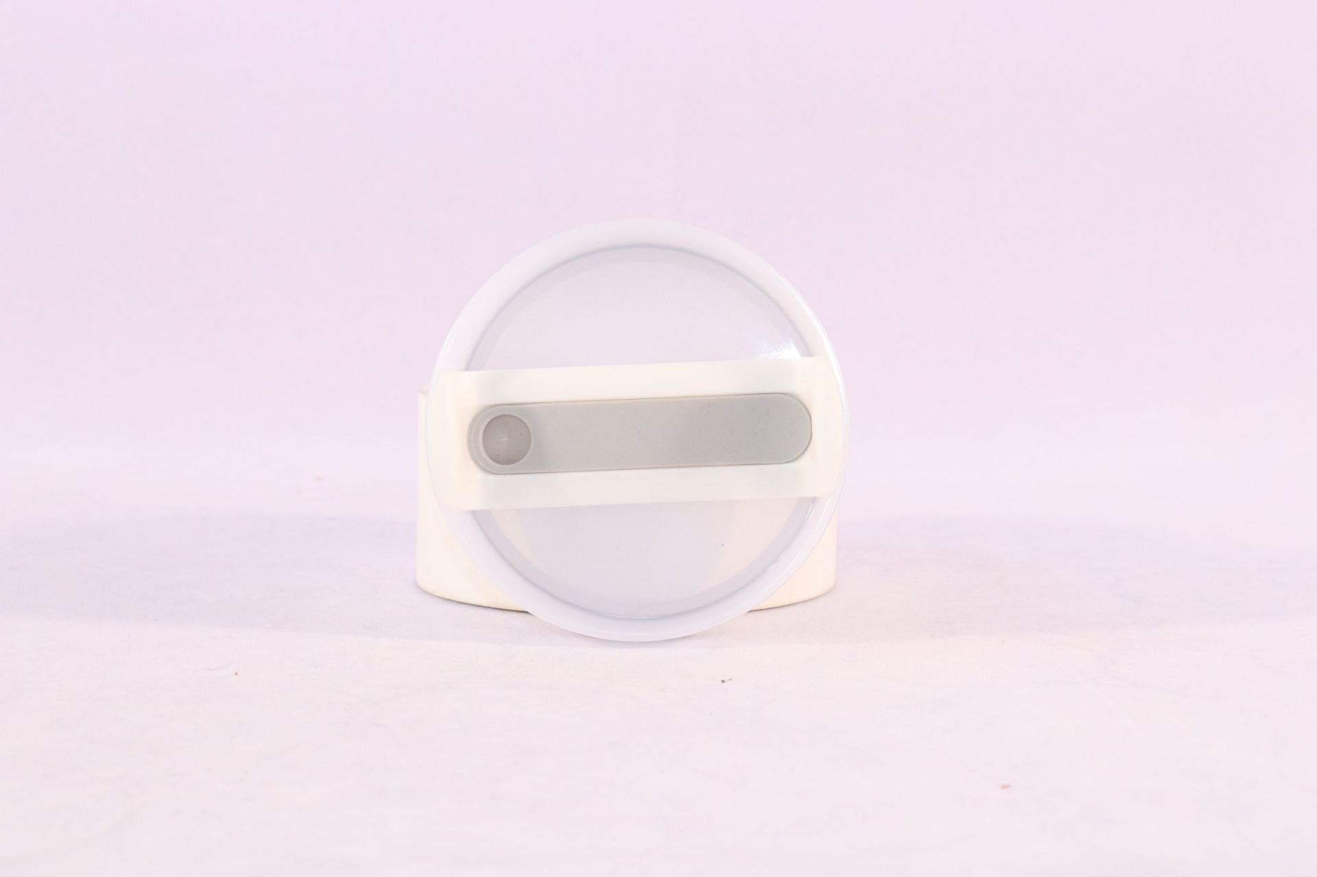 Round white object with a central gray component on a light purple background
